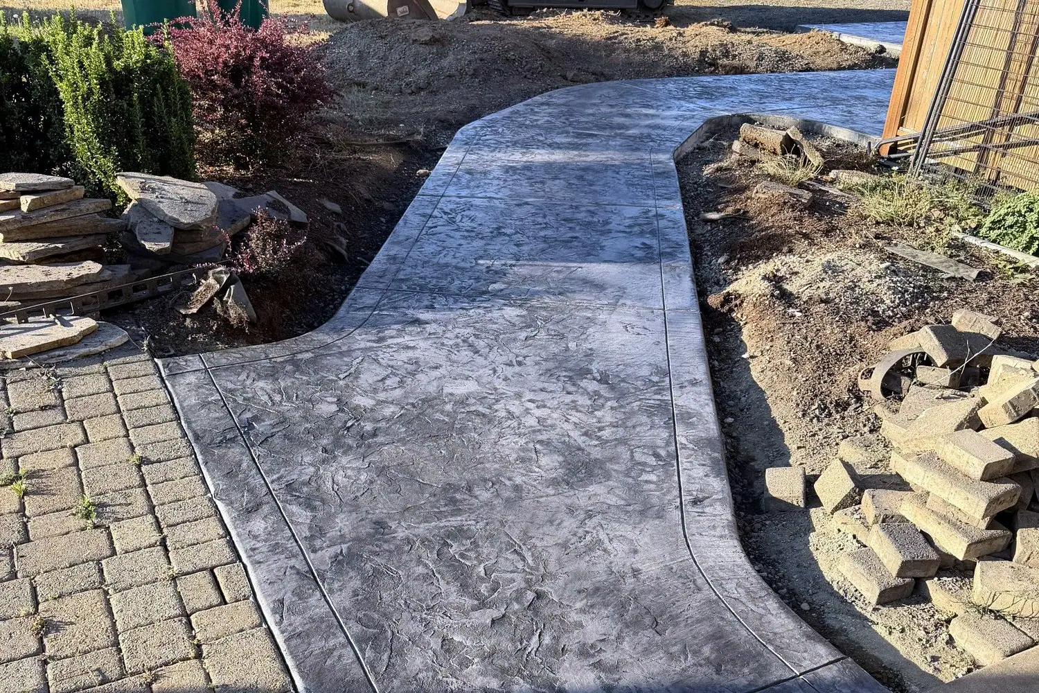 Curved stamped concrete walkway next to a paver patio